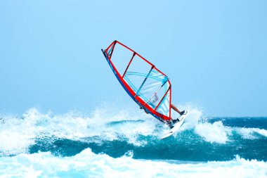 Su sporları: Güneşli bir yaz öğleden sonrasında kırmızı ve turuncu yelkenli rüzgar sörfçüsü.