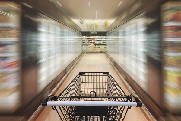 Supermarket aisle with empty shopping cart — Stock Photo, Image