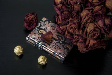 Koyu arkaplanda romantik bir kompozisyon. Kırmızı kuru gül çiçekleri ve defter..