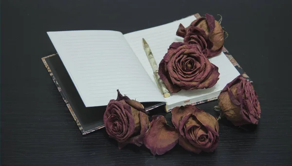 Romantic vintage composition on dark background. Red dry rose flowers and notebook. — Stock Photo, Image