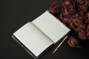 Kırmızı kuru gül çiçekleri ve defter. Koyu arkaplanda romantik klasik kompozisyon.