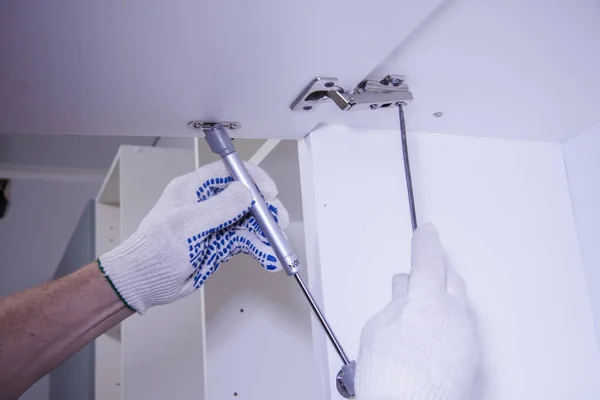 Mãos de trabalho masculinas em luvas brancas com uma chave de fenda. Montagem de armários de cozinha . — Fotografia de Stock