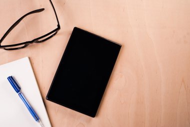 Tablet boş ekran siyah gözlüklü ve ofis ahşap masa üstünde not etmek,