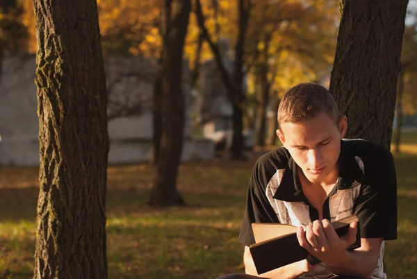 Молодой человек читает книгу в осеннем парке , — стоковое фото