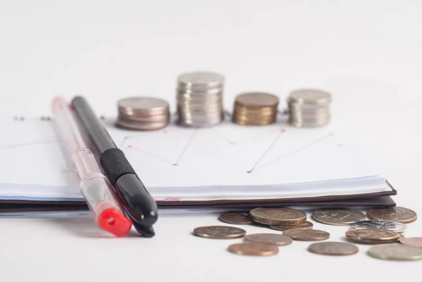 Fechamento pilha de moedas, caneta e bloco de notas no fundo branco . — Fotografia de Stock