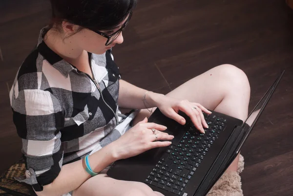 Giovane donna brunetka seduta sul pavimento con le gambe incrociate e digitando sul computer portatile — Foto Stock