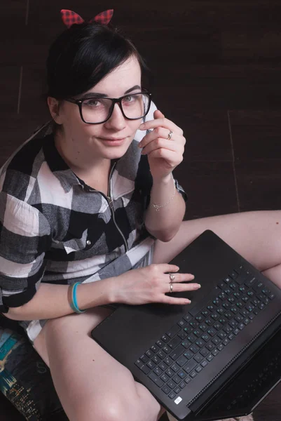 Young woman brunetka sitting on the floor with crossed legs and typing on the laptop — Stock Photo, Image