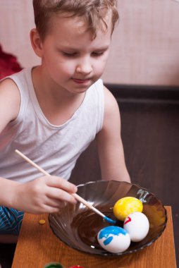 Küçük bir çocuk yumurta Paskalya, renkli boya ve fırça arifesinde boyar.,