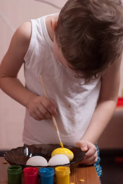 Un petit garçon peint les œufs à la veille de Pâques, peintures colorées et brosse , — Photo