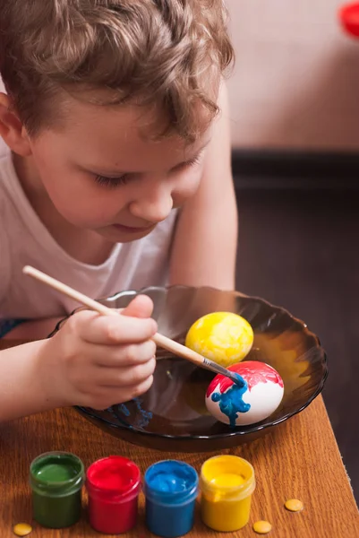 Un petit garçon peint les œufs à la veille de Pâques, peintures colorées et brosse , — Photo