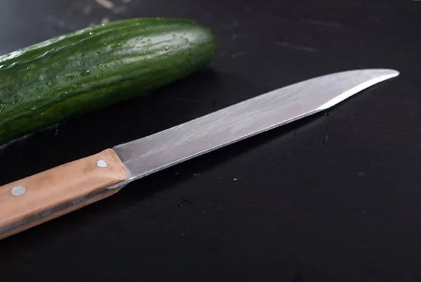 Concombres frais et couteau sur une planche à découper noire — Photo
