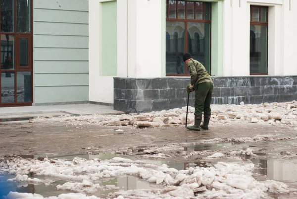Un hombre limpia la acera de hielo, el trabajador de los servicios municipales en la calle, a finales de primavera , —  Fotos de Stock