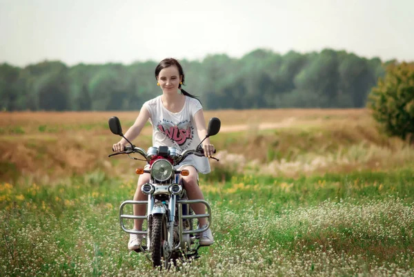 Kobieta w t-shirt jeździ w polu na motorower. — Zdjęcie stockowe