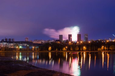 Gölün üzerinde havai fişek, şehrin gece silüeti,