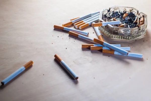 Un cendrier sale avec des mégots de cigarette éparpillés cigarettes filtrantes sur une table en bois , — Photo