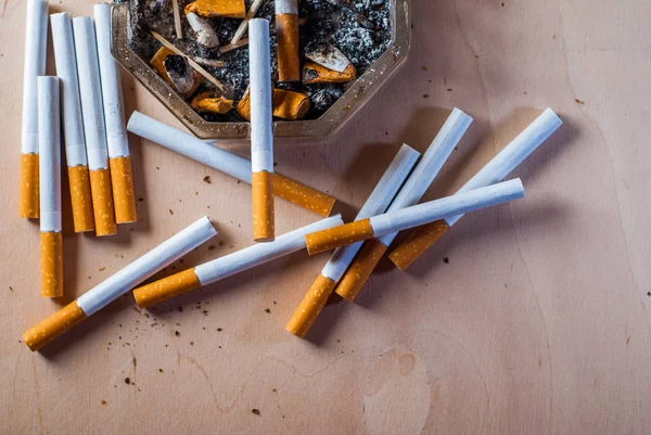 Un cendrier sale avec des mégots de cigarette éparpillés cigarettes filtrantes sur une table en bois , — Photo