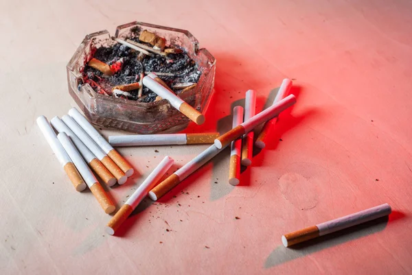 Un cendrier sale avec des mégots de cigarette éparpillés cigarettes filtrantes sur une table en bois , — Photo