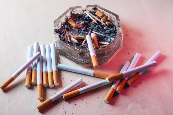 Un cendrier sale avec des mégots de cigarette éparpillés cigarettes filtrantes sur une table en bois , — Photo