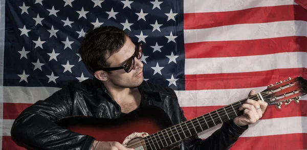 A man plays the guitar on the backdrop of the American flag — Stock Photo, Image