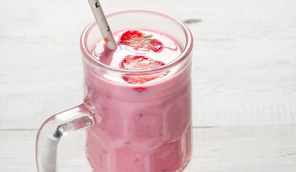 Un batido de fresa en un bolígrafo de cristal sobre una vieja mesa de madera . — Foto de Stock