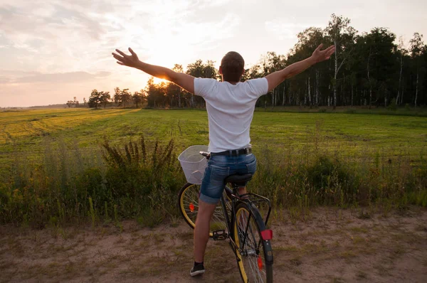 Pôr do sol e feliz jovem em uma bicicleta, o conceito de felicidade e sucesso — Fotografia de Stock