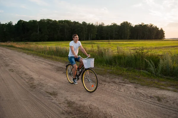 Хлопець їде на велосипеді уздовж заміської дороги на заході сонця , — стокове фото