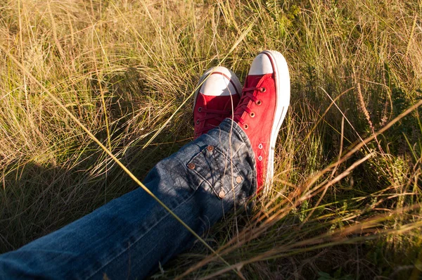 Pernas em sapatos vermelhos na grama para descansar durante a caminhada — Fotografia de Stock