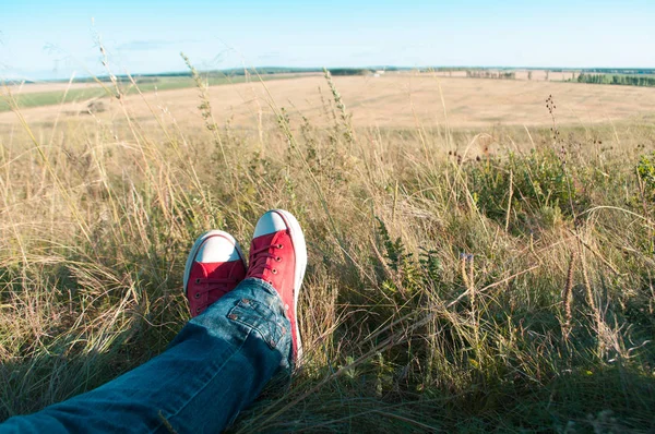 Nogi w czerwone buty na trawie do odpoczynku podczas wędrówki — Zdjęcie stockowe
