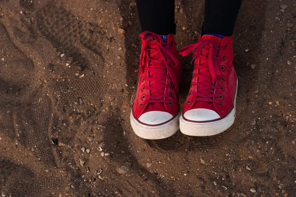 Sneakers rosse sulla sabbia, piedi femminili in scarpe rosse — Foto Stock