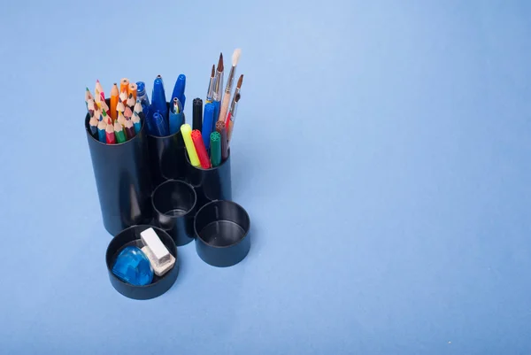 Soportes negros para suministros de oficina con ellos sobre un fondo azul , — Foto de Stock