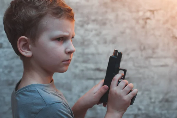 Menino com arma na mão contra uma parede de tijolo , — Fotografia de Stock