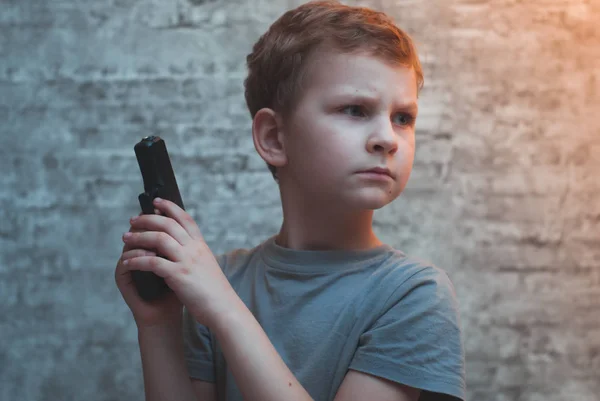 Pojke med en pistol i handen mot tegelväggar, — Stockfoto