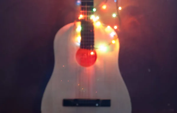 Fondo difuminado abstracto, una guitarra acústica envuelta en guirnalda — Foto de Stock