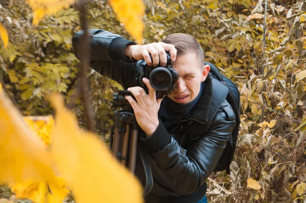 Photographer in a leather jacket shoots in autumn Park, — Stock Photo, Image