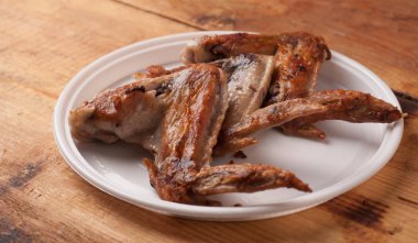 Ahşap masa üzerinde beyaz bir plastik tabak kızarmış tavuk kanatları,