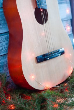 Ahşap arka planda Noel ışıkları olan akustik gitar, müzik aletlerinin Noel indirimi,