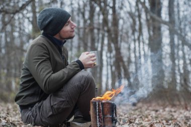 Bir adam ormandaki demir bardaktan çay içer ve tadını çıkarır. Dışarıda mutlu bir adam,