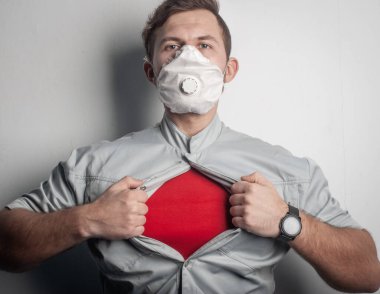 Kırmızı tişörtlü ve tıbbi maskeli bir süper kahraman göğsünü yırtarak virüs kurbanlarına yardım etmeye çalışıyor.