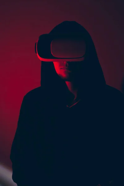 A hacker in the VR glasses in red light, the gamer in the virtual space, — Stock Photo, Image