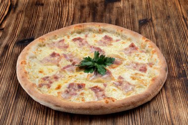Eritilmiş peynirli sıcak İtalyan pizzası ve ahşap arka planda domuz pastırması şeritleri. 