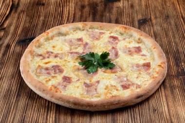 Eritilmiş peynirli sıcak İtalyan pizzası ve ahşap arka planda domuz pastırması şeritleri. 