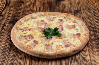 Eritilmiş peynirli sıcak İtalyan pizzası ve ahşap arka planda domuz pastırması şeritleri. 