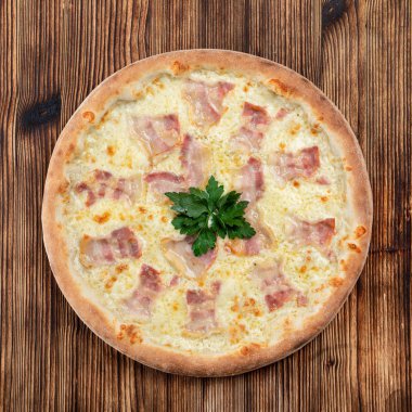 Eritilmiş peynirli sıcak İtalyan pizzası ve ahşap arka planda domuz pastırması şeritleri. 