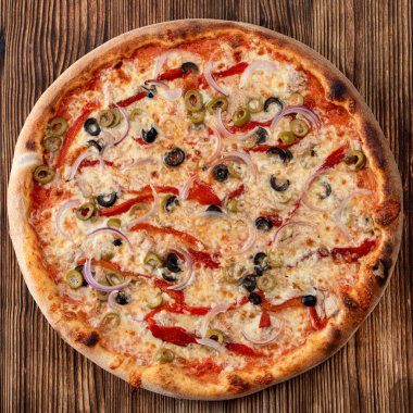 Yuvarlak pizzanın kırmızı soğanlı, siyah ve yeşil zeytinli, erimiş peynirli ve arka planda ketçaplı üst görüntüsü.