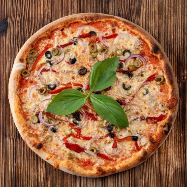 Yuvarlak pizzanın kırmızı soğanlı, siyah ve yeşil zeytinli, erimiş peynirli ve arka planda ketçaplı üst görüntüsü.