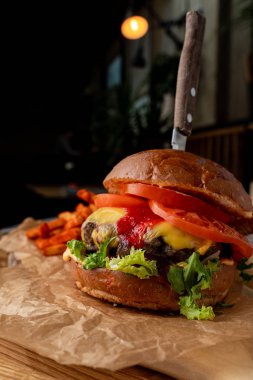 Çedar peynirli sulu sığır burger ve siyah arka planda patates kızartması.