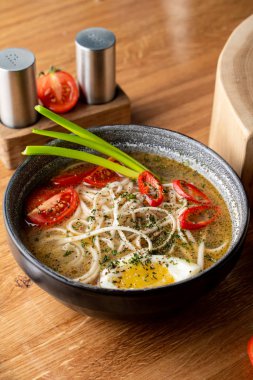 Haşlanmış yumurta, domates ve ahşap masada kırmızı biber ile sıcak tavuk çorbası.