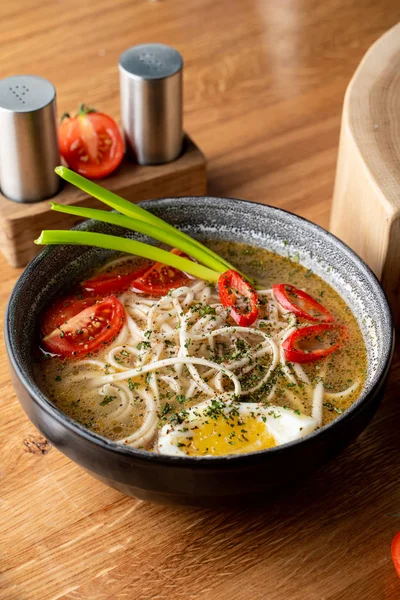 Haşlanmış yumurta, domates ve ahşap masada kırmızı biber ile sıcak tavuk çorbası.