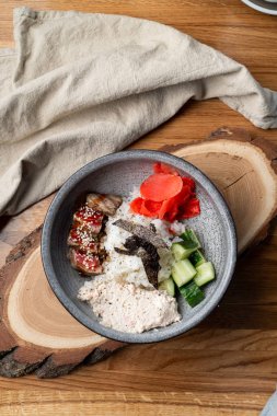 Bıçak ve çatalla ahşap masada pirinç, zencefil ve salatalık dolu yılan balığı kasesi.