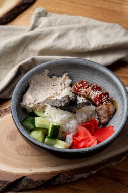 Bıçak ve çatalla ahşap masada pirinç, zencefil ve salatalık dolu yılan balığı kasesi.